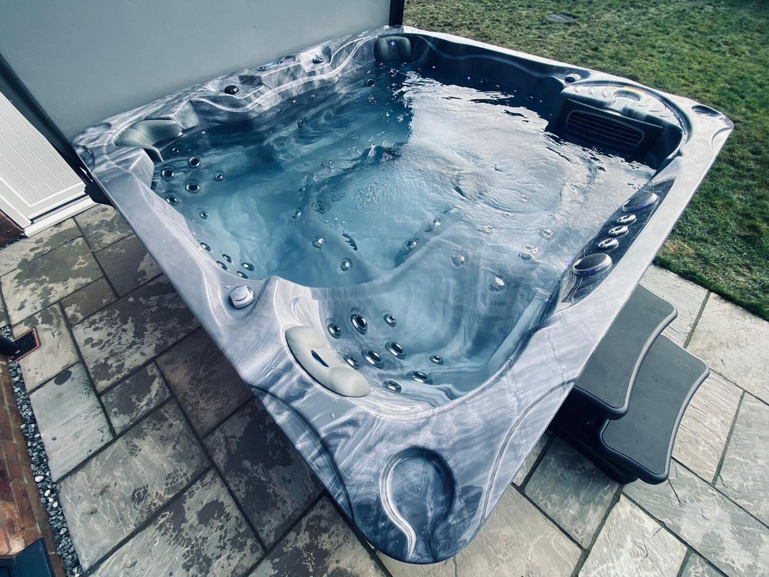 Hot tub with swirling blue water, grey marble-like exterior, on a brick patio.