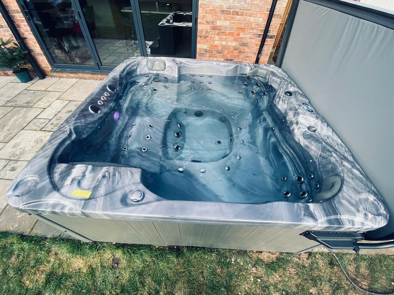 A filled triangular hot tub with grey and black marbled interior, outdoors on a patio.