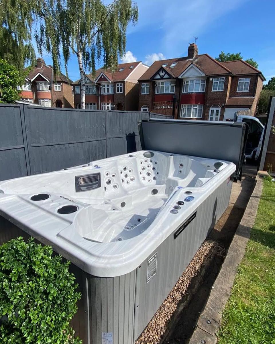 Hot tub in a backyard, with partial cover open. Grey fence, houses in background.