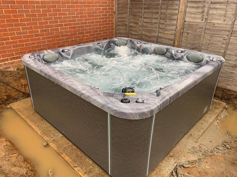 Hot tub with bubbling water in an outdoor setting, next to a brick wall and wooden fence.