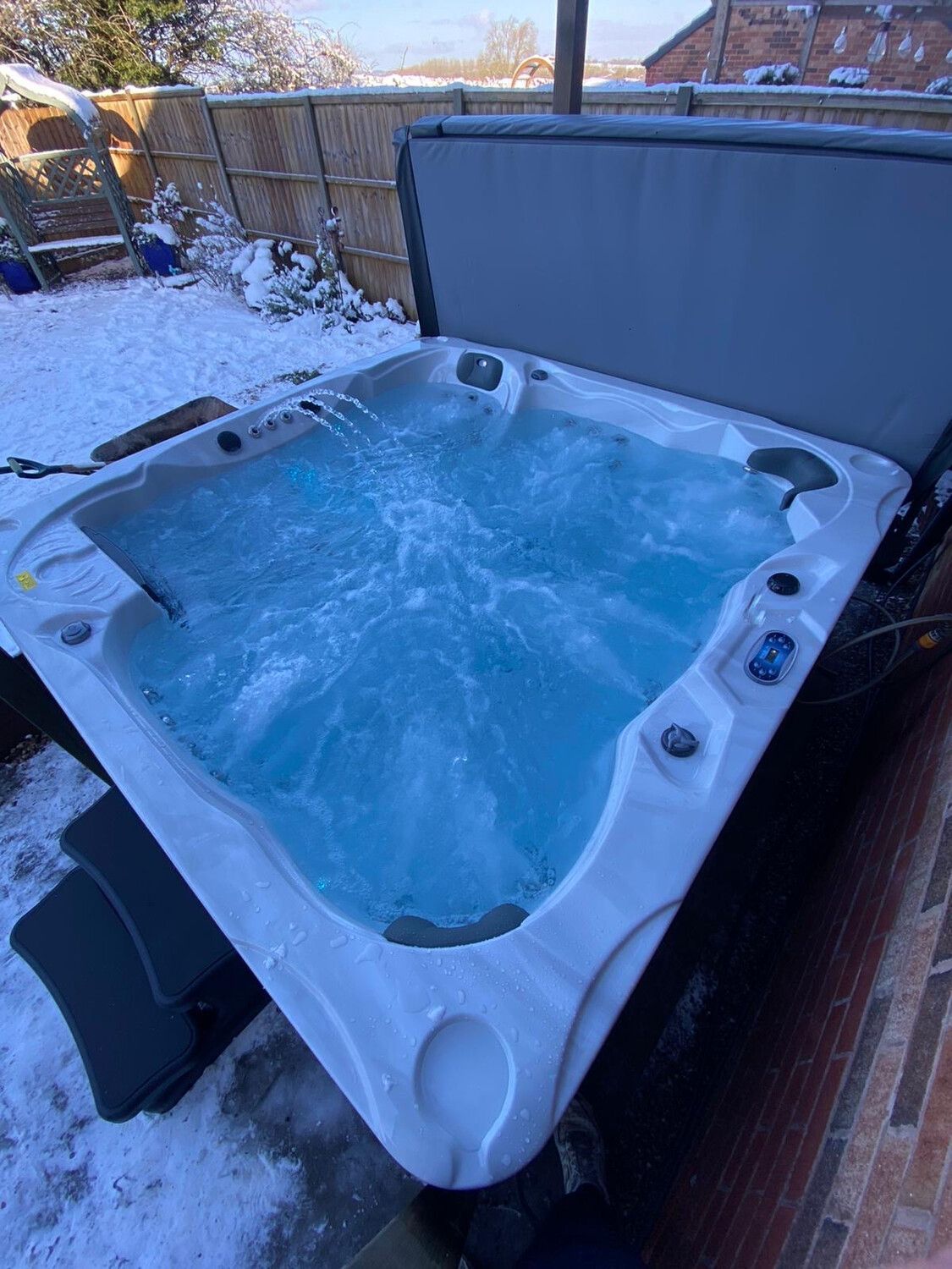 Hot tub with blue water outdoors, surrounded by snow. Lid open, jets running.