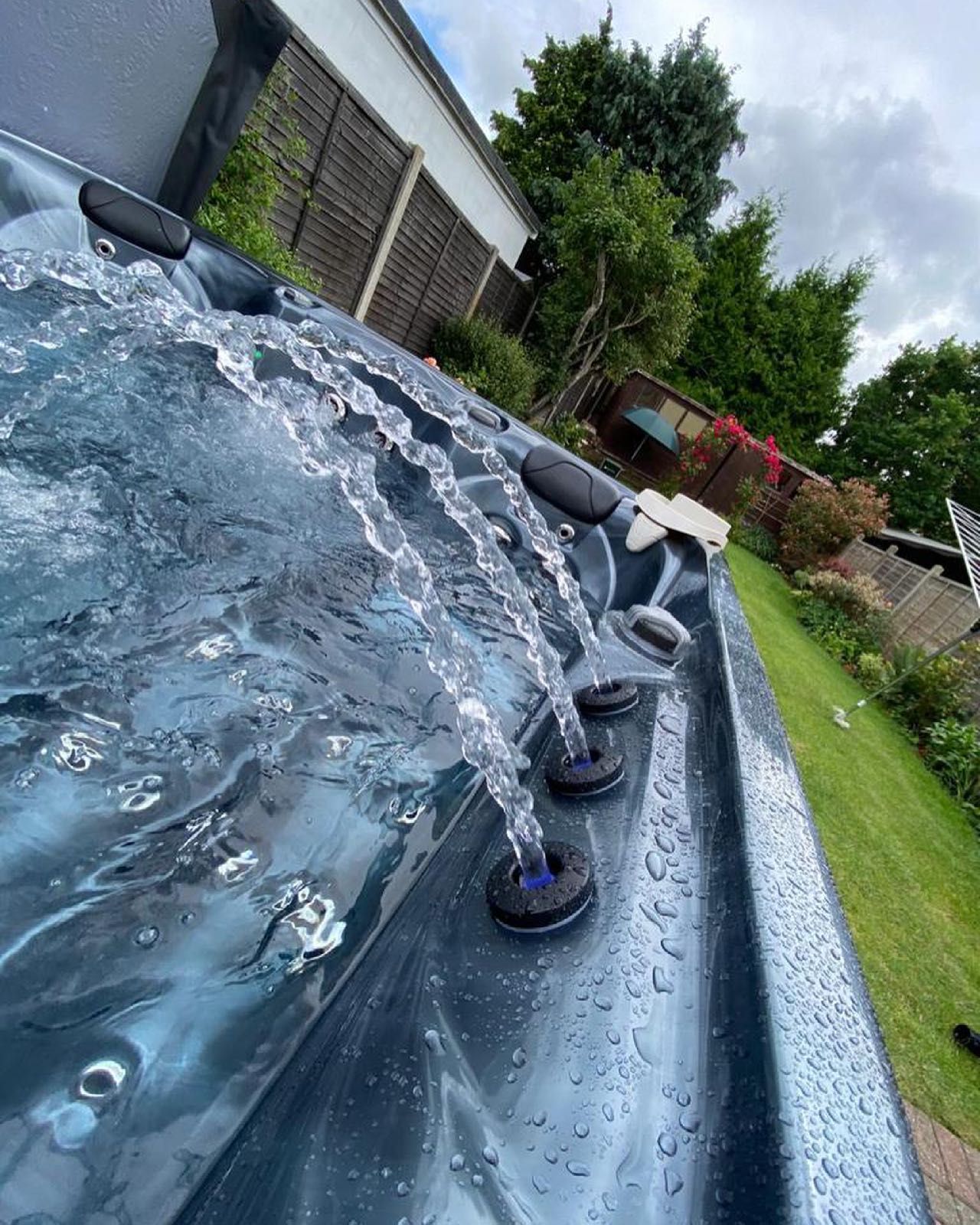 Hot tub with water jets spraying outward in a green outdoor setting.