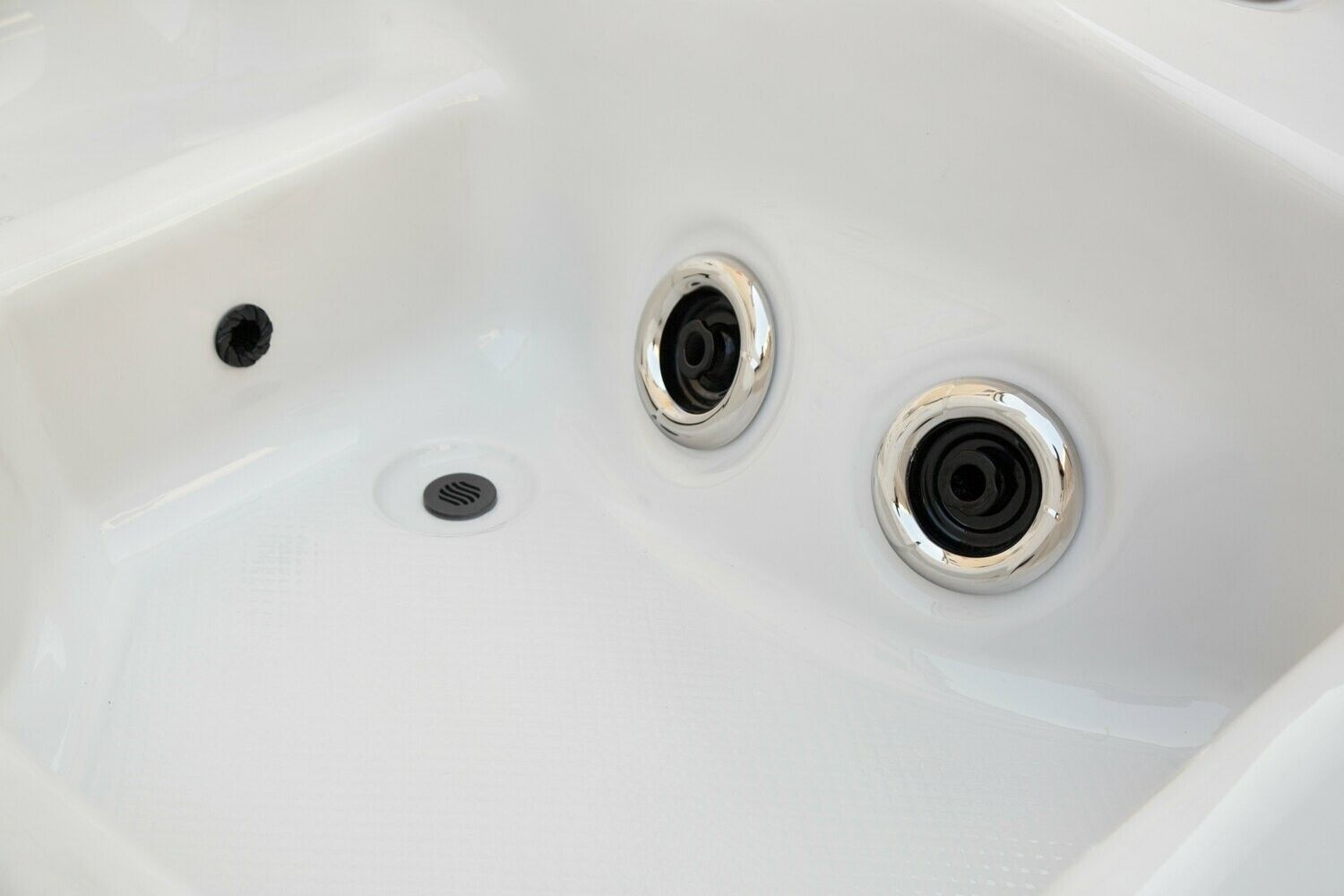 Close-up of a white hot tub interior, featuring black jets and glossy surface.