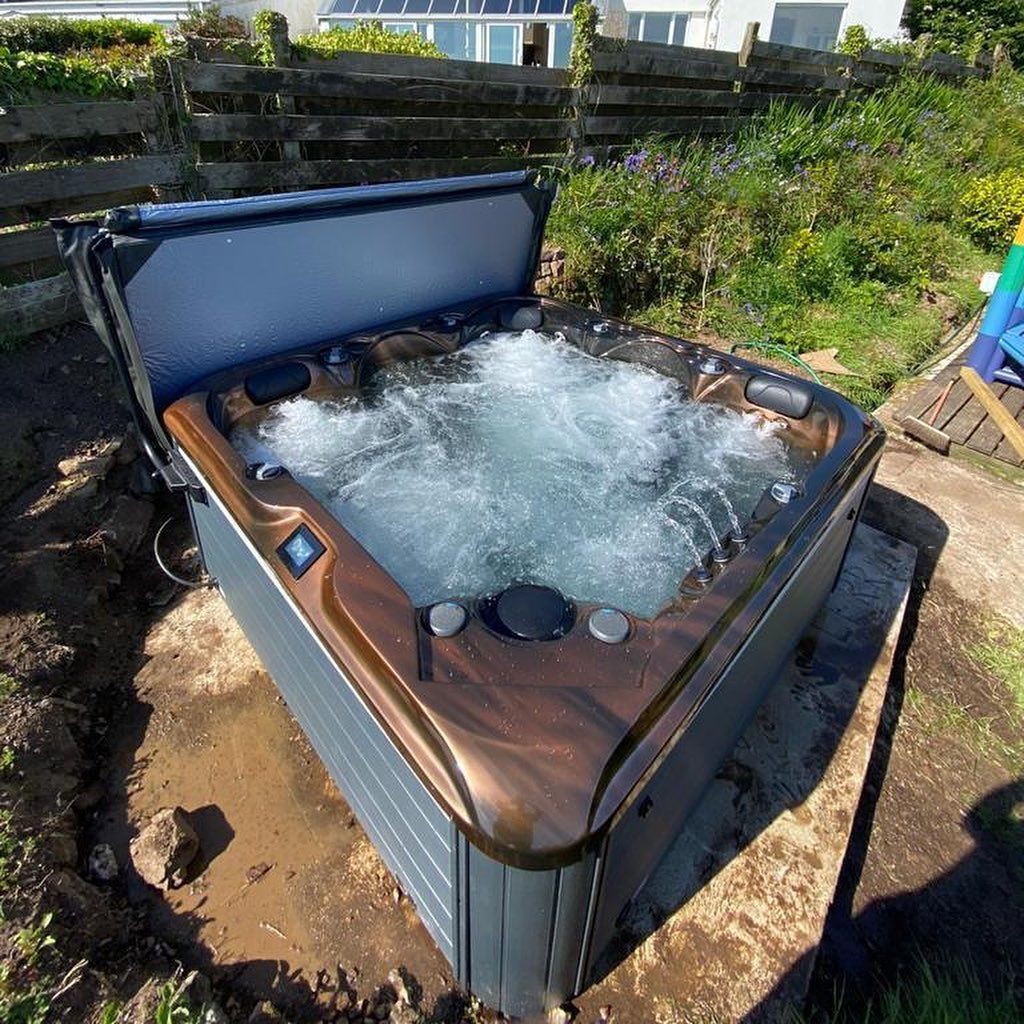 A hot tub with bubbly water, cover partially open, in a garden setting. Brown and gray tones.