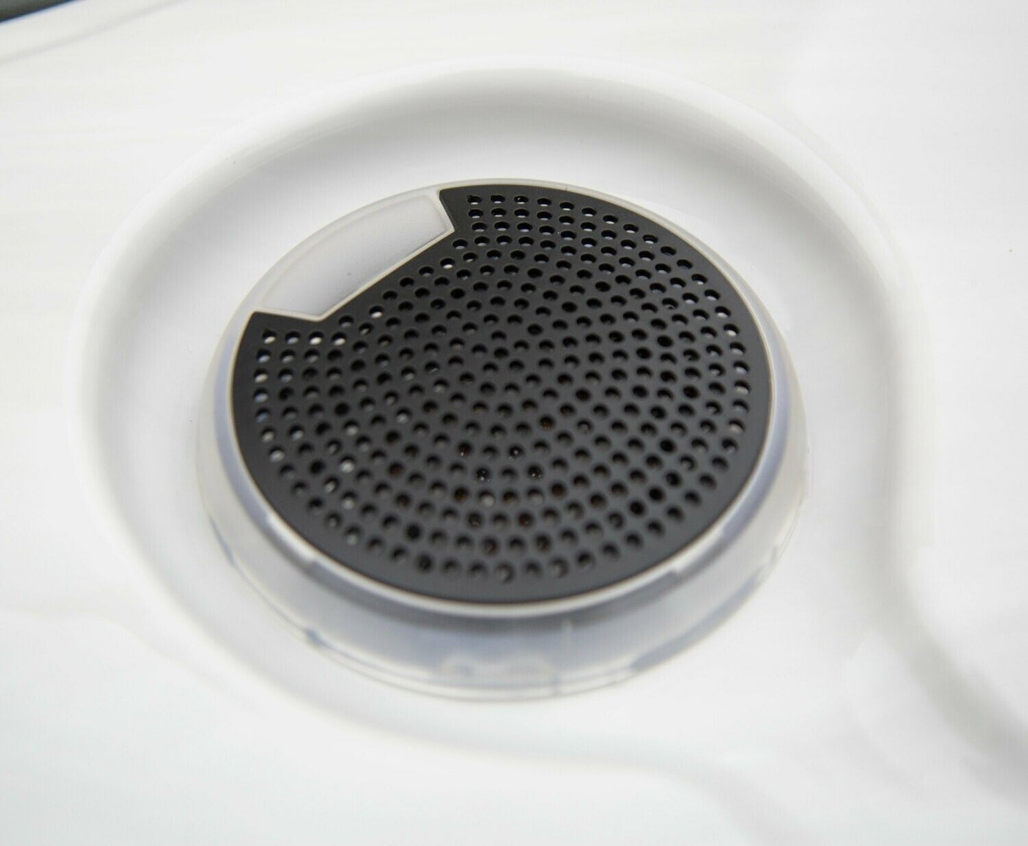 Close-up of a white sink drain with a black, perforated cover and a white plastic rim.