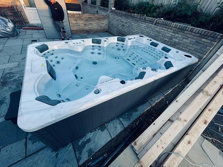 Large hot tub filled with water, positioned on a patio, with a person standing nearby.