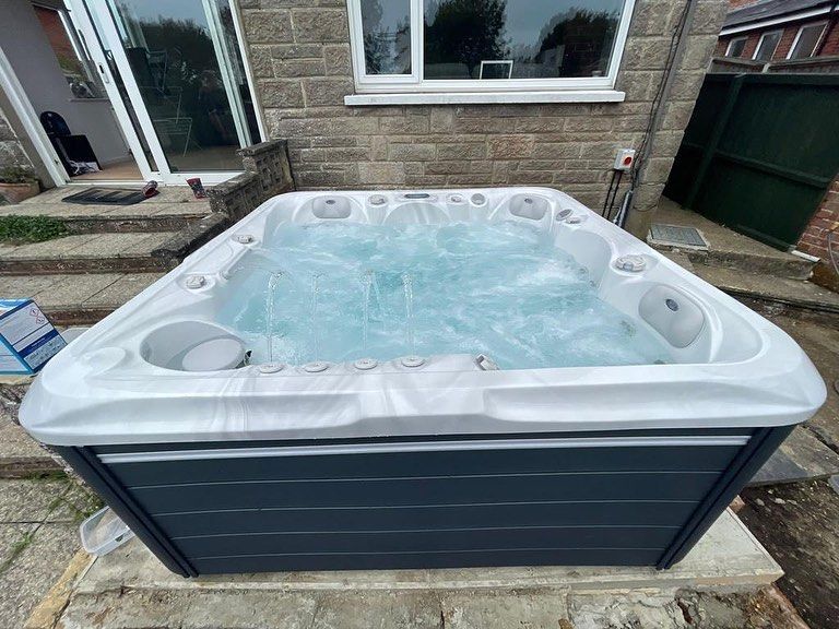 Hot tub filled with water, outside on a stone patio, gray and white, bubbling with jets.