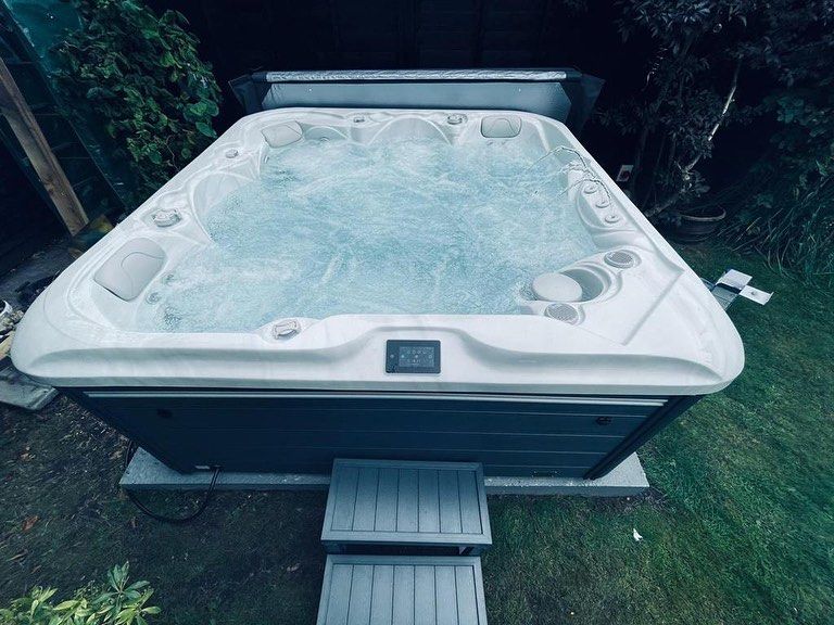 Hot tub in a backyard with bubbling water, dark blue base, and grey steps.