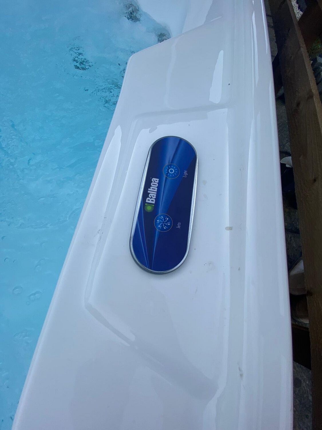 White hot tub edge with a blue control panel, partially filled with blue water.