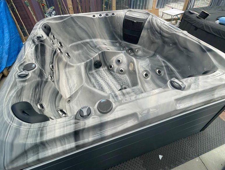 A new, empty hot tub with gray and black marbled interior, sitting outdoors in a sunny setting.