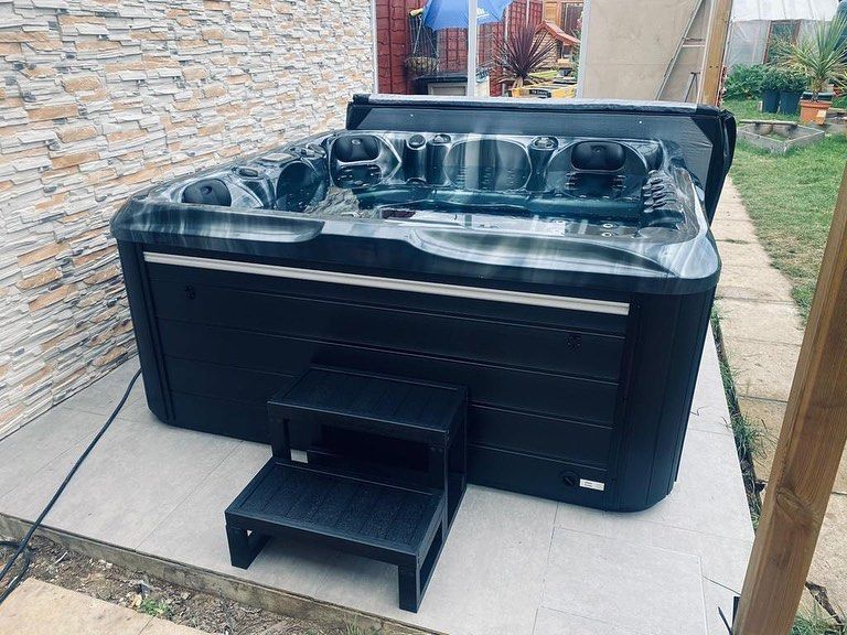 Hot tub on a patio, with steps leading up to it. Black exterior, gray interior with seats.