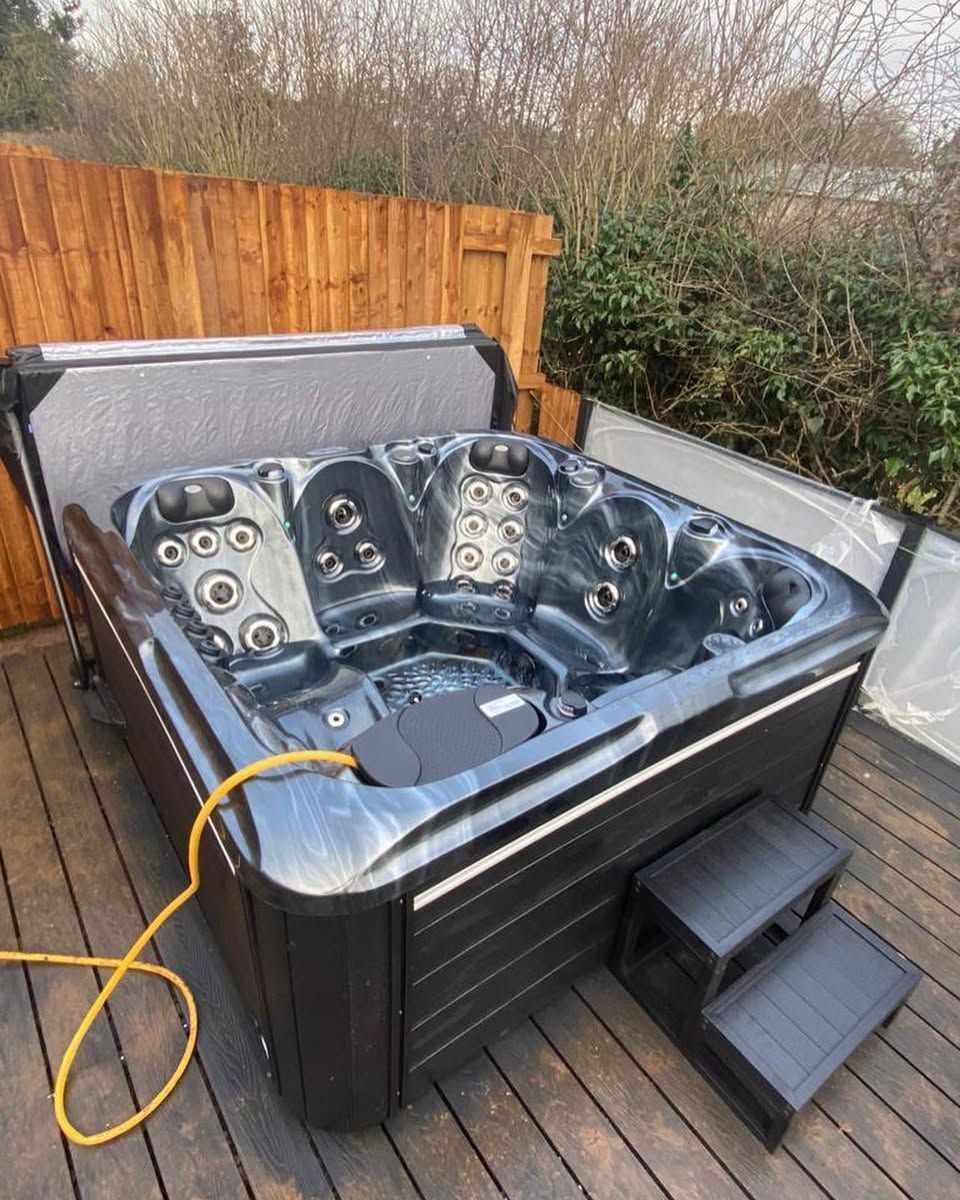 Hot tub on a wooden deck with a wooden fence. The tub is black with steps and a yellow cord.