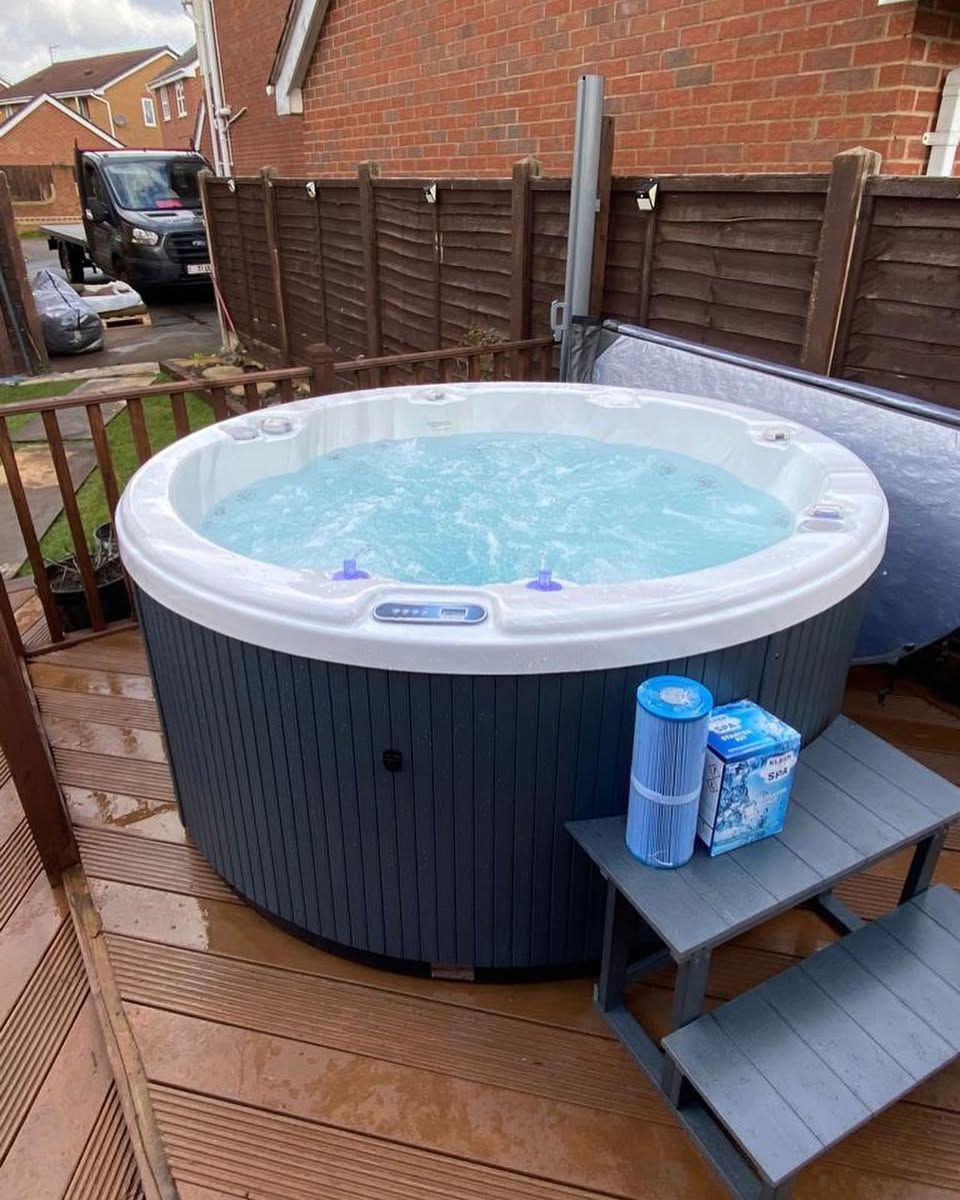 Round hot tub filled with water on a wooden deck.  Filters and a small stepstool are nearby.