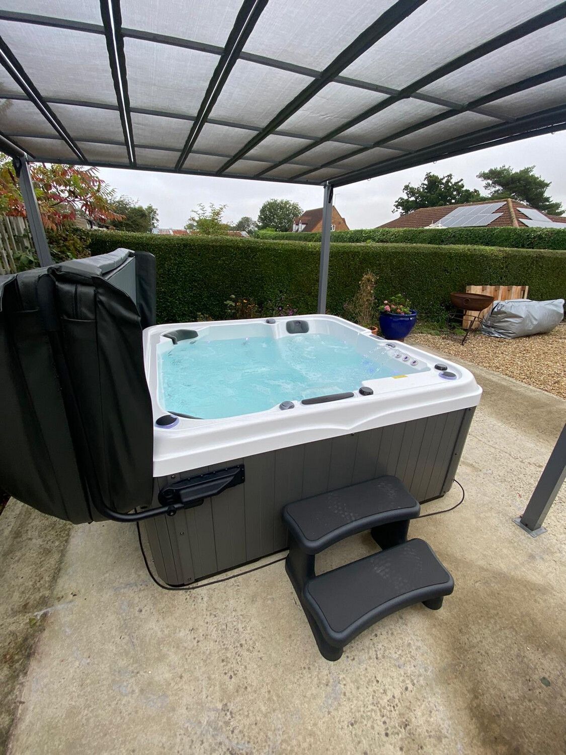 Hot tub under a canopy, with steps, cover open, filled with water, on patio.
