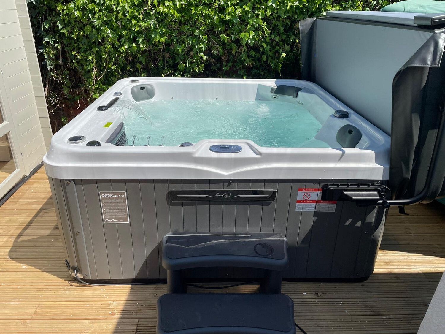 Hot tub with bubbling water on a wooden deck, partially covered, with steps.