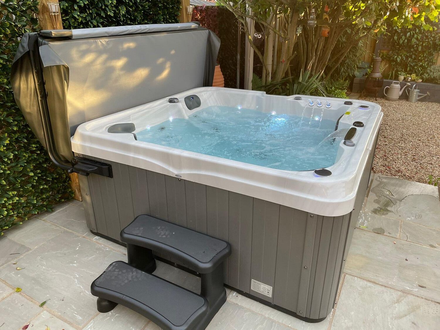 Hot tub on a patio, gray exterior, cover open. Steps in front.
