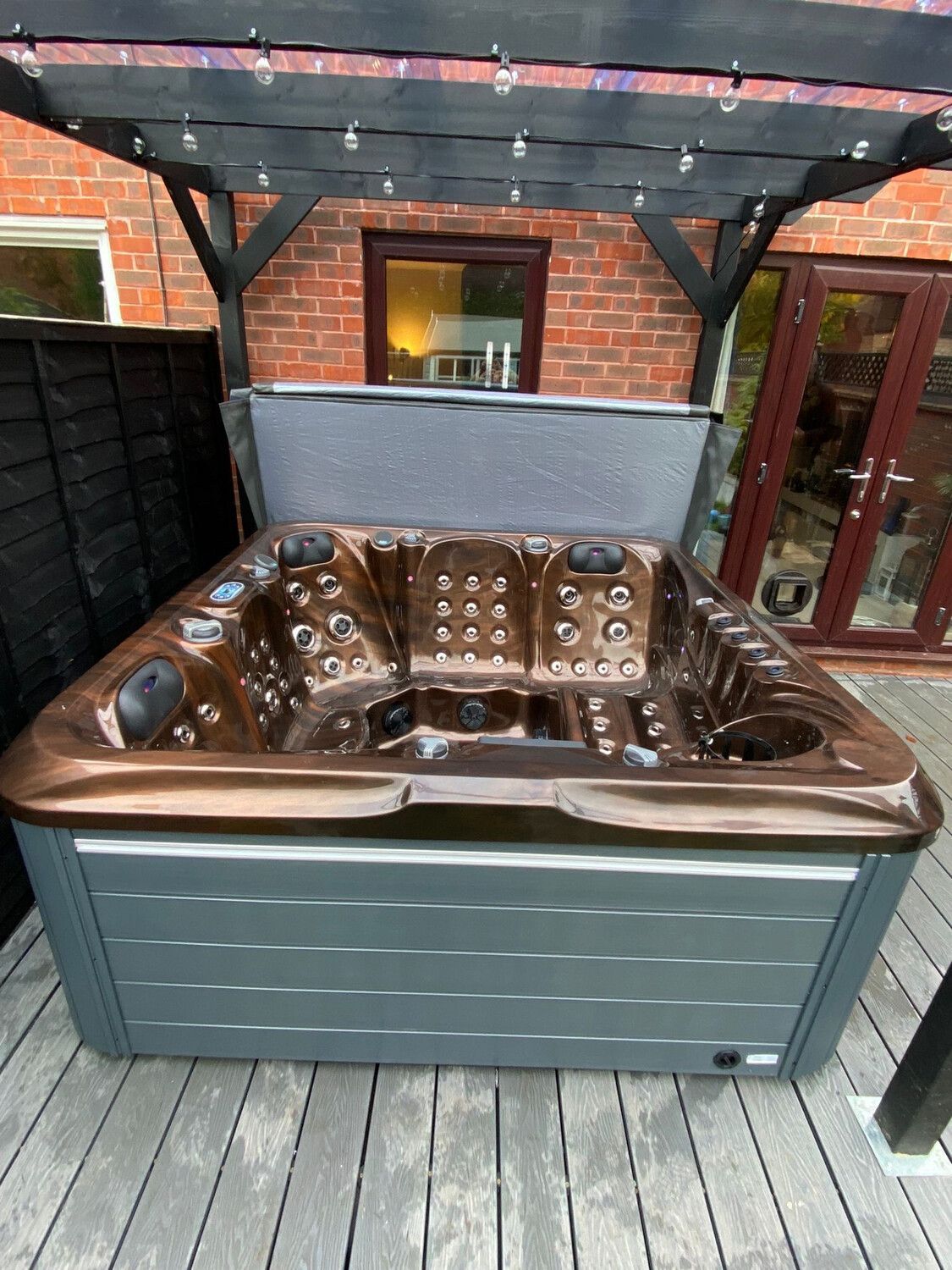 Hot tub with bronze interior and gray exterior under a black pergola.