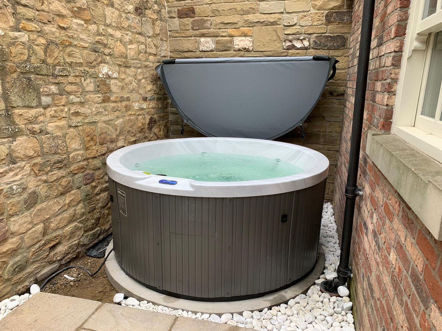 Round outdoor hot tub with open cover, next to brick wall.