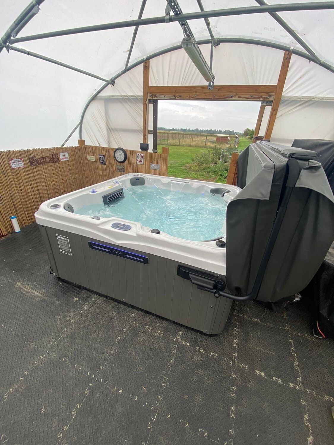 Hot tub bubbling inside a white-framed enclosure with an open door looking out at a field.