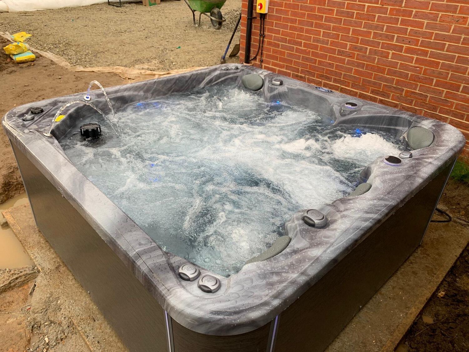 A square hot tub with bubbling water sits outside a brick building.