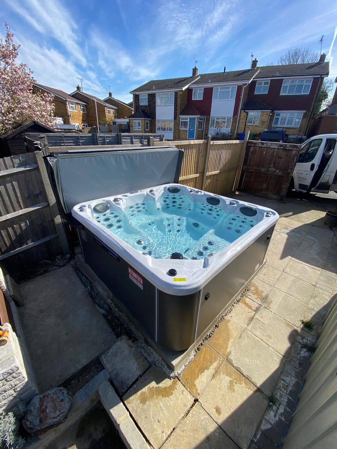 Hot tub in a backyard with blue water and cover partially open.