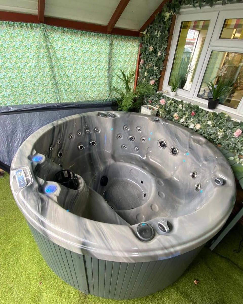Round hot tub with gray and white marbled interior, set on green grass, under a covered patio.