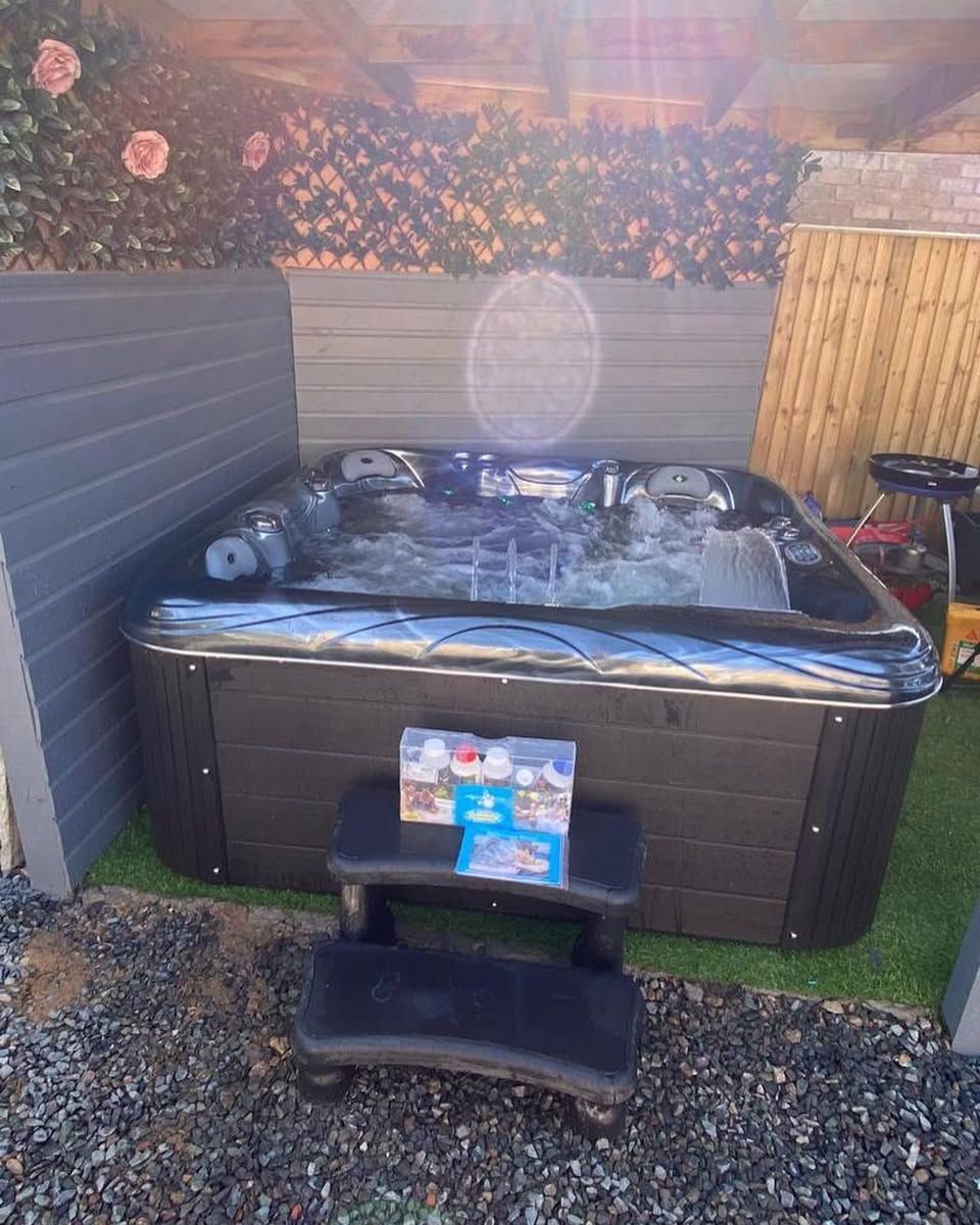 Hot tub with dark gray exterior, steps, and greenery in a backyard setting.