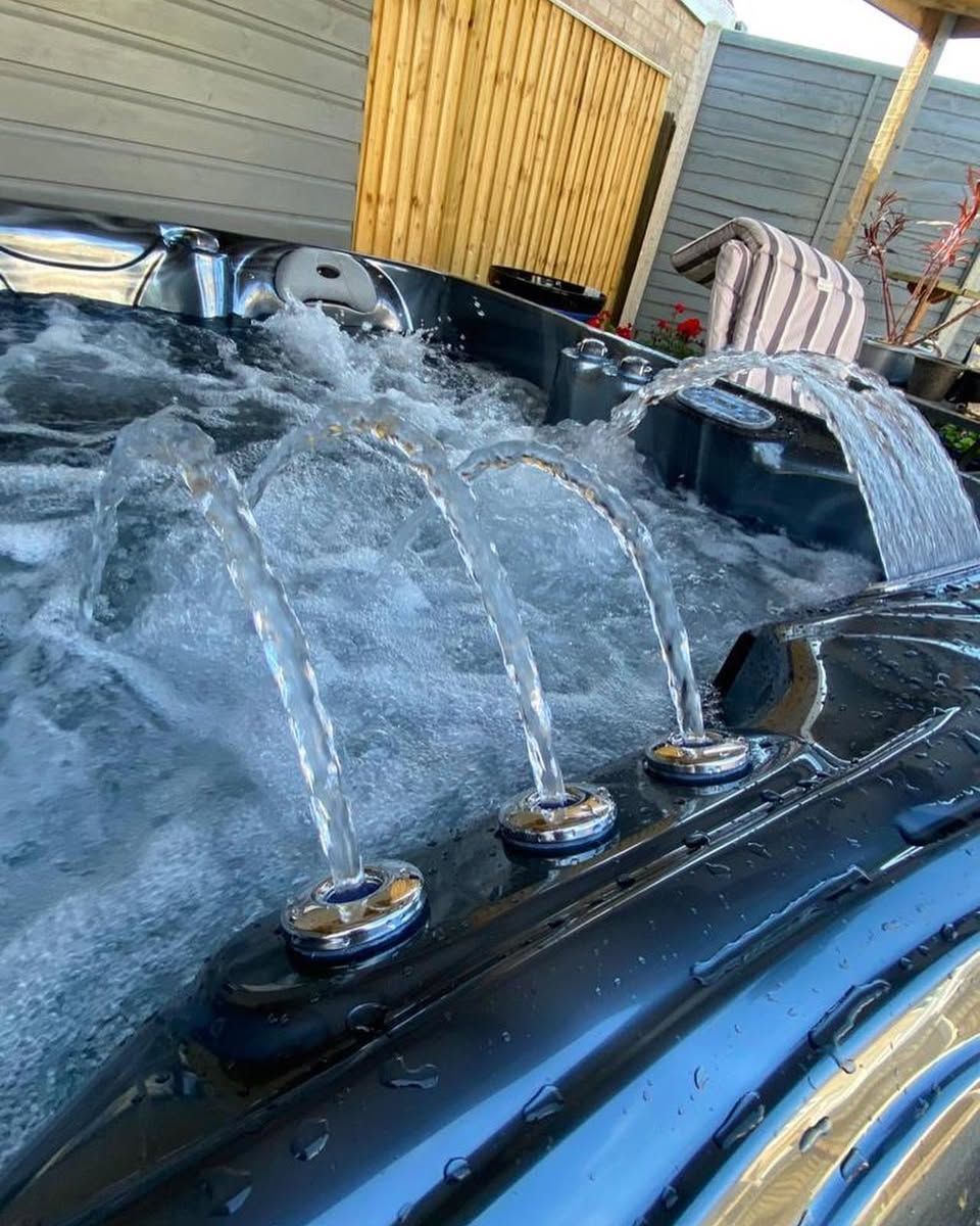 Hot tub with water jets, filled with bubbling water, outdoors next to wooden fence.
