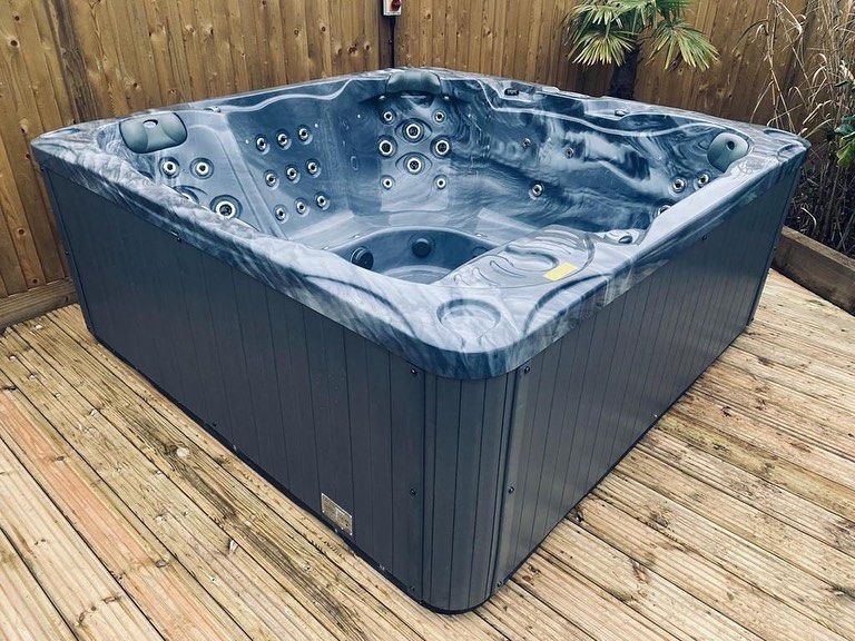 A square, gray hot tub on a wooden deck, against a wooden fence.