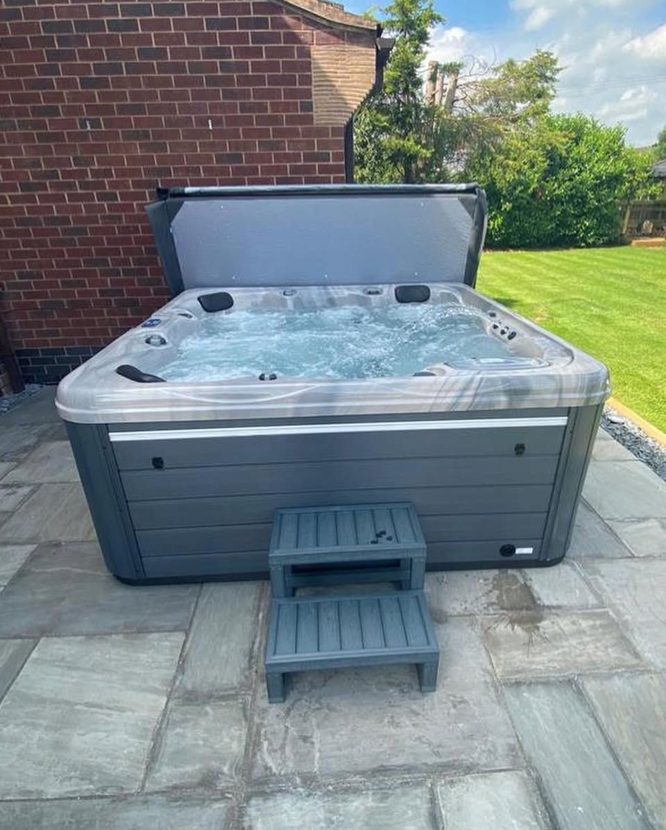 Dark gray hot tub with bubbling water, cover open, on stone patio, step stool in front.