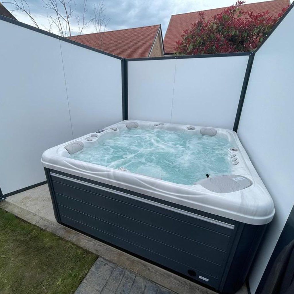 Hot tub surrounded by white privacy panels, bubbling water, gray exterior, outdoor setting.