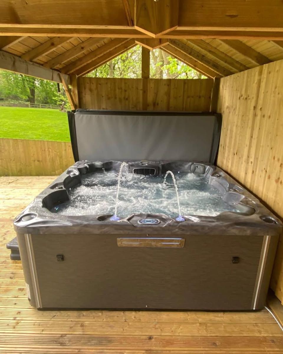 Hot tub with two fountains under a wooden gazebo on a deck. The tub is filled with water.