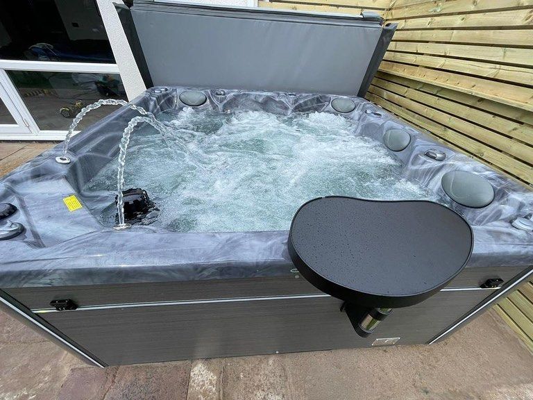 Hot tub with water jets, black cover partly open, set on patio beside a wooden fence.