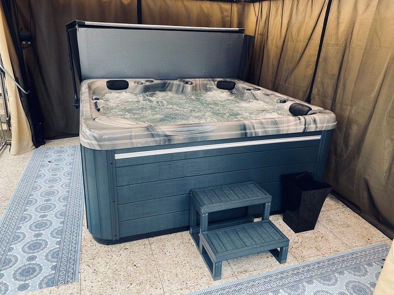 Hot tub with open cover, steps, and trash can on a patio with a rug.