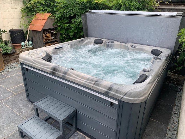 Hot tub in a backyard with bubbling water, grey exterior, and step.
