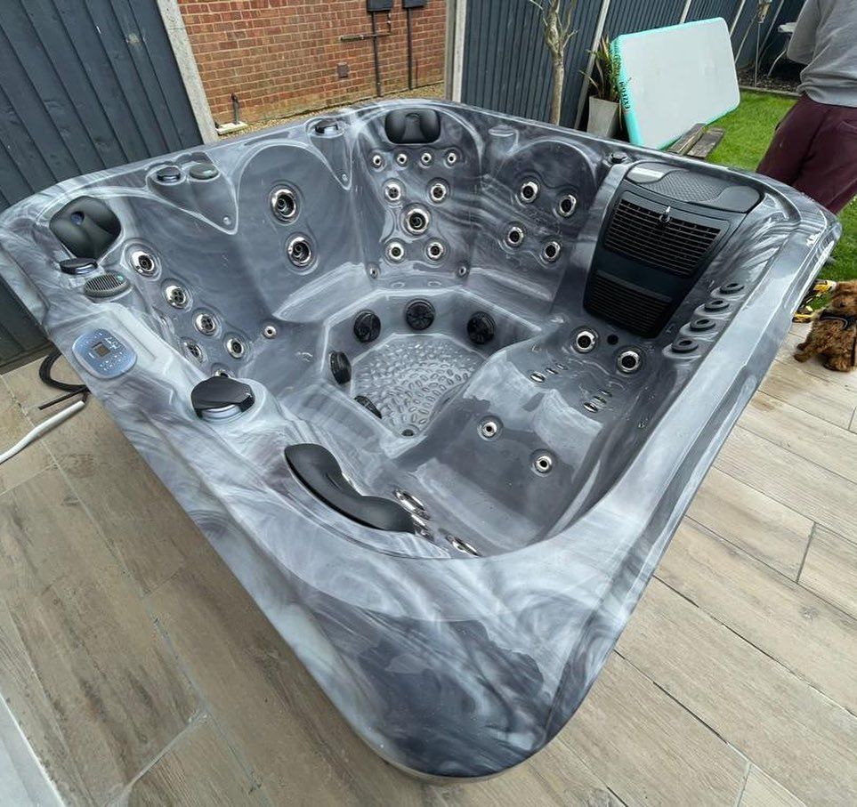 A gray and white hot tub with multiple jets, on a tiled patio.