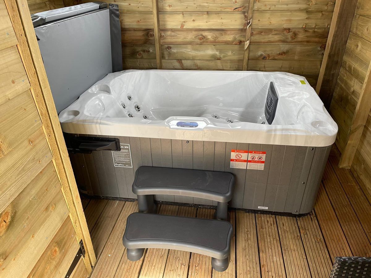 Hot tub in a wooden shed with steps. The hot tub is grey with a closed cover.