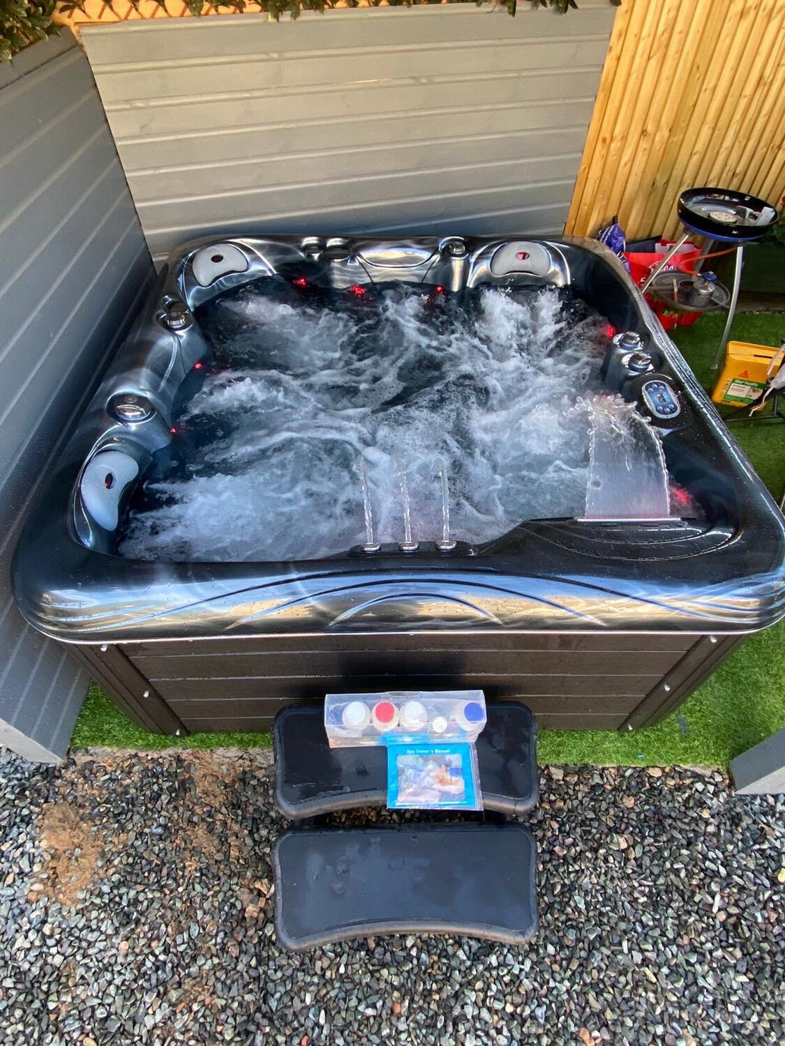 Hot tub with bubbling water, set in a backyard. Features a black exterior, blue jets, and a step stool.