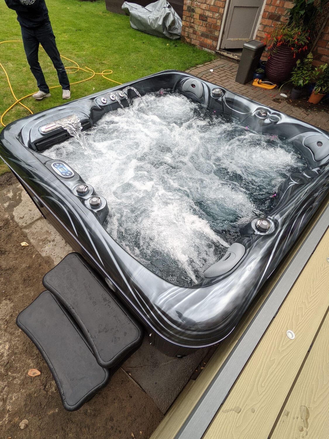Hot tub with bubbling water, dark gray exterior, steps, and person nearby.