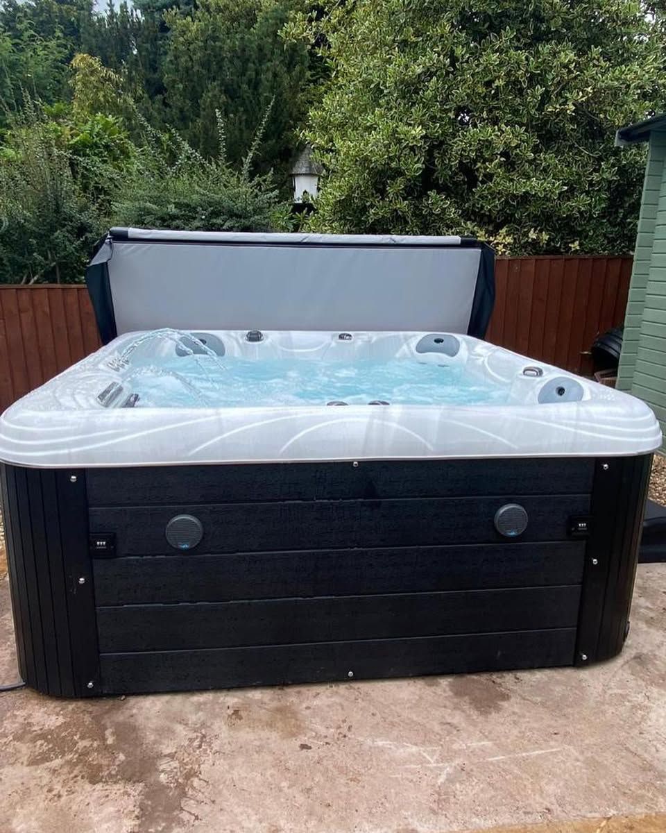 Hot tub with black siding and open cover, surrounded by greenery.