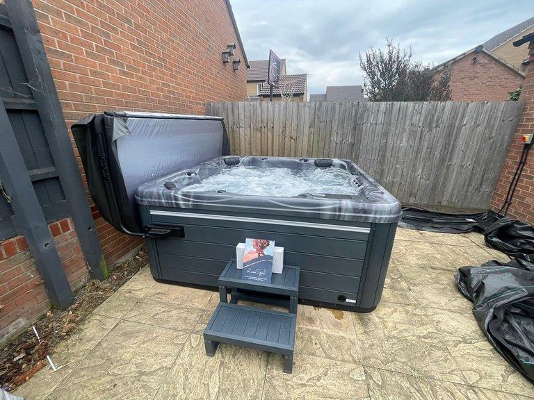 Hot tub with open cover, on a patio next to a brick wall and fence.