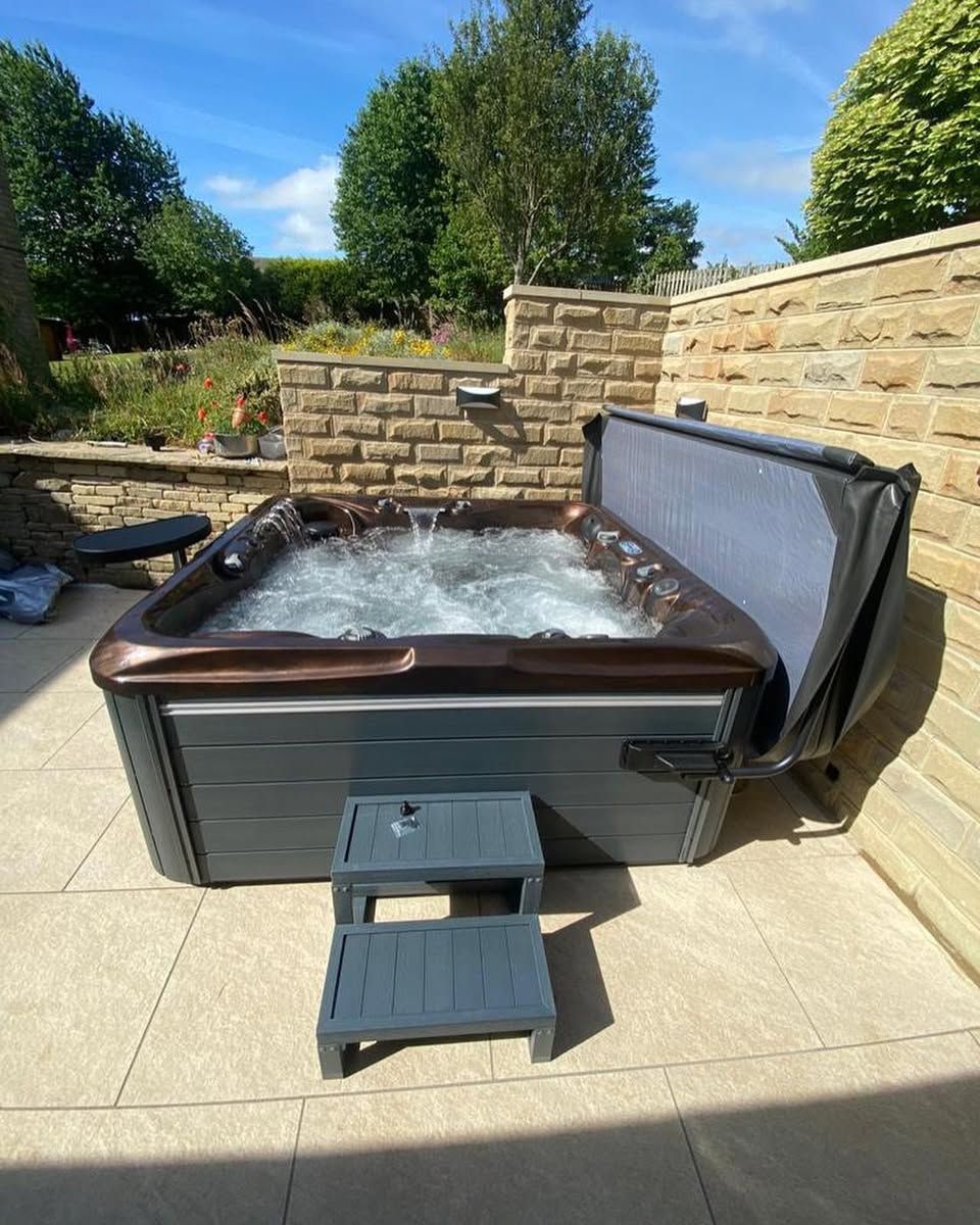 Hot tub with water jets on a patio, partially covered by a dark blue cover, with gray steps.