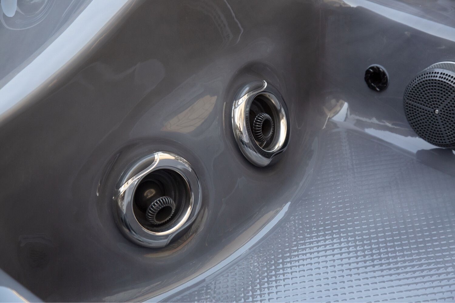 Close-up of two spa jets in a gray spa, showing metallic nozzle details, set in a gray textured surface.