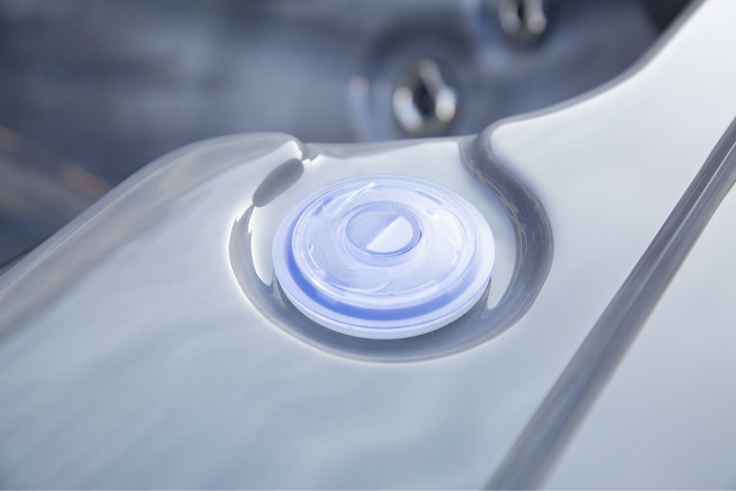 Close-up of a white hot tub with a lit, blue jet.