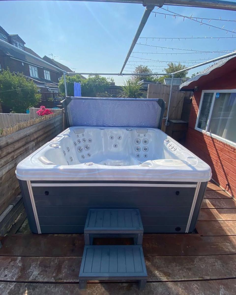 A hot tub on a wooden deck, gray and white with a step stool, beneath a clothesline.