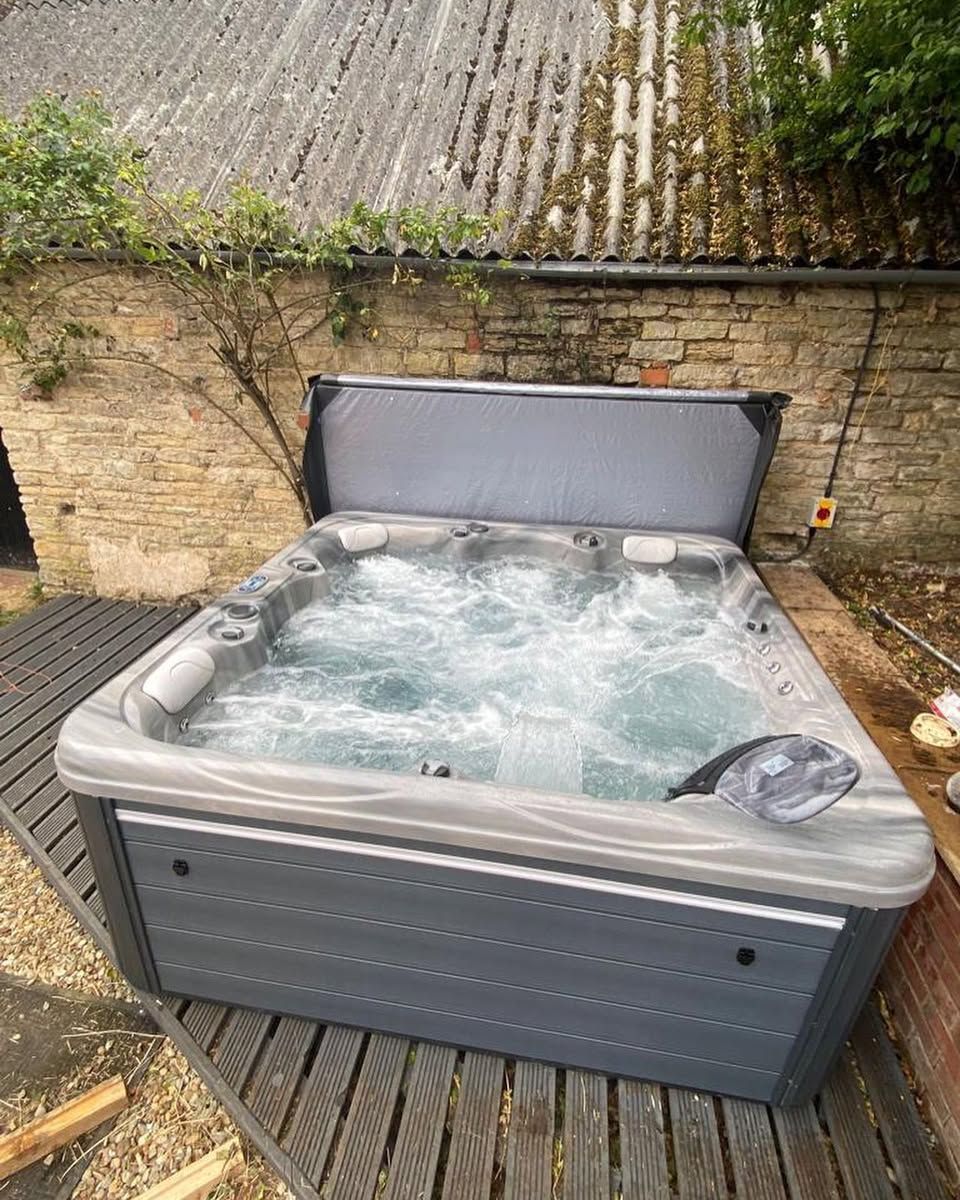 Hot tub with open cover, bubbling water, and grey exterior, placed outdoors on a wooden deck.