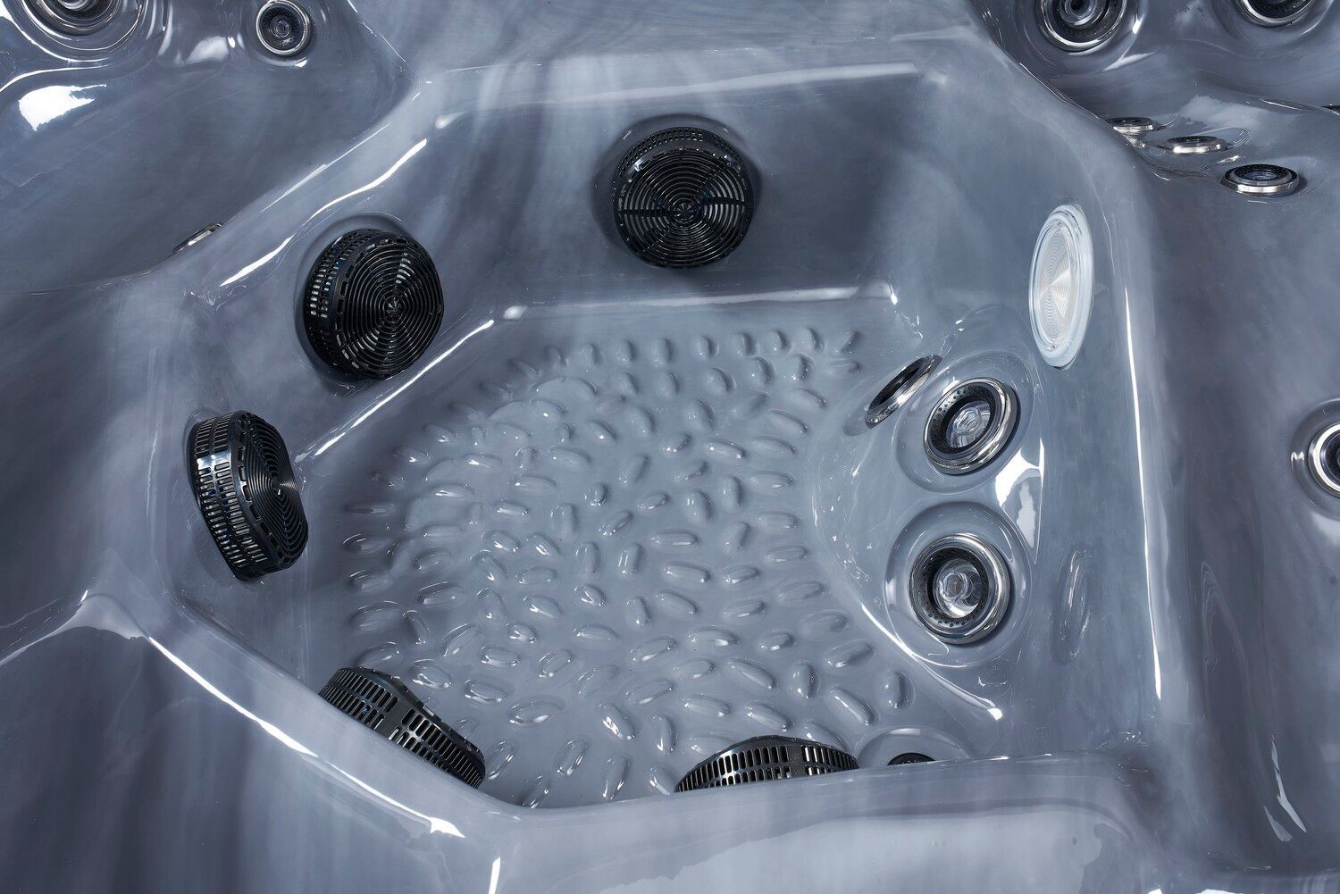 Interior of a gray hot tub with black jets and a textured floor.