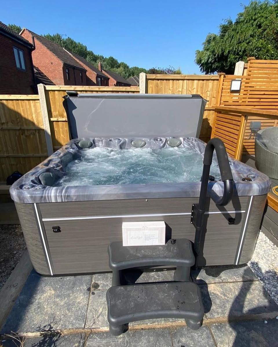 Hot tub with bubbling water, steps, and handrail in a backyard setting.
