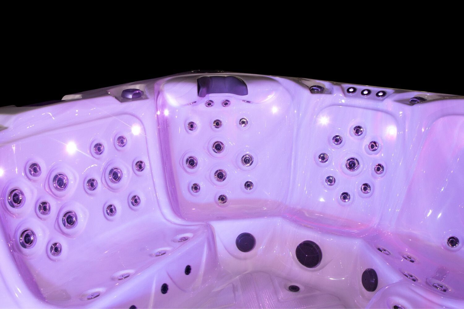 Interior of a lit hot tub with multiple jets, glowing purple against a black background.