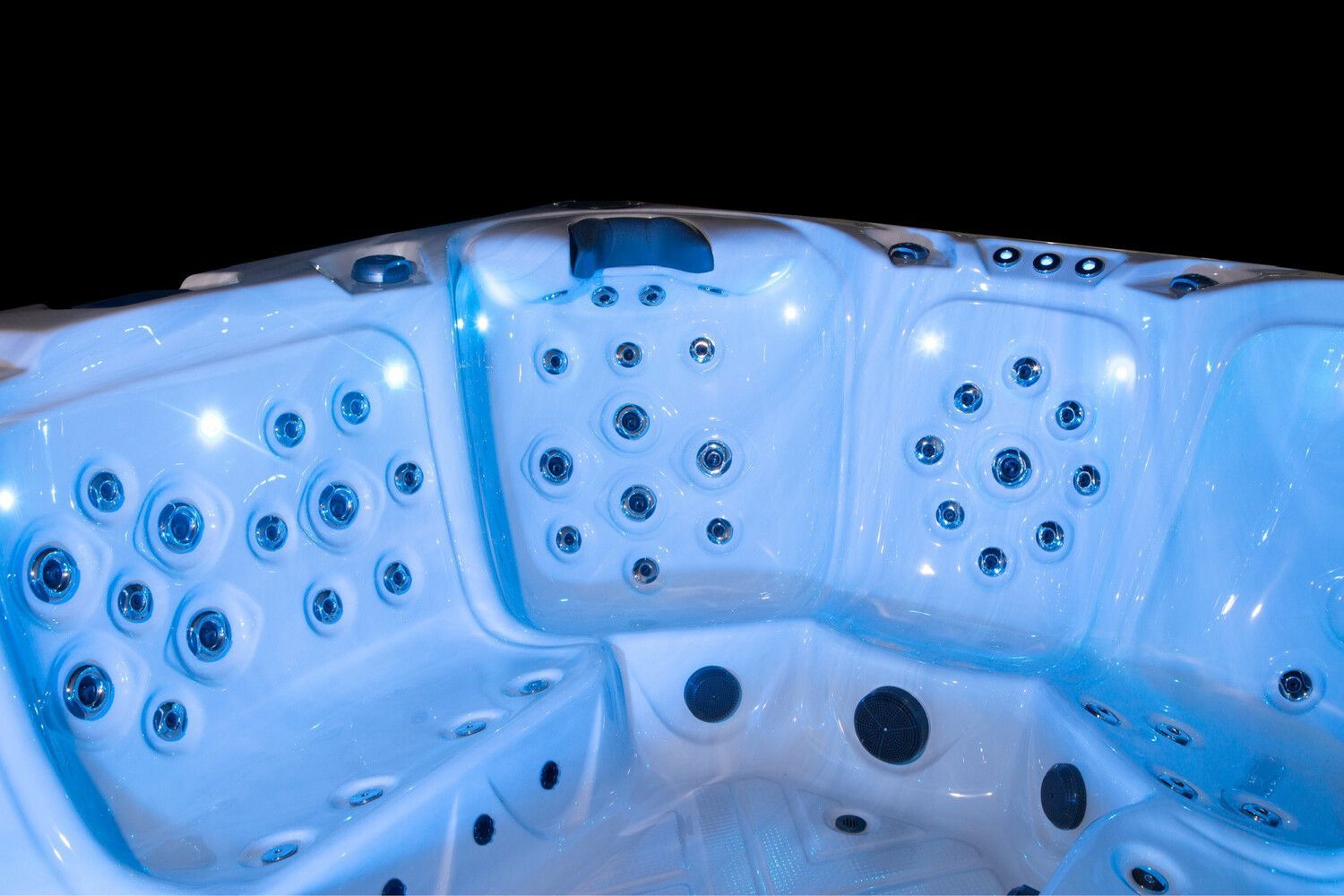 Interior of a lit white hot tub with numerous jets against a black background.